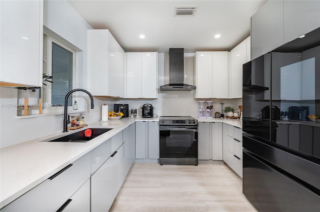 kitchen featuring white cabinets, sink, wall chimney exhaust hood, light wood-type flooring, and electric range oven