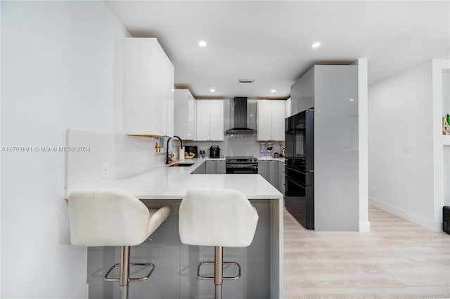 kitchen featuring white cabinetry, sink, electric range, wall chimney range hood, and a breakfast bar area