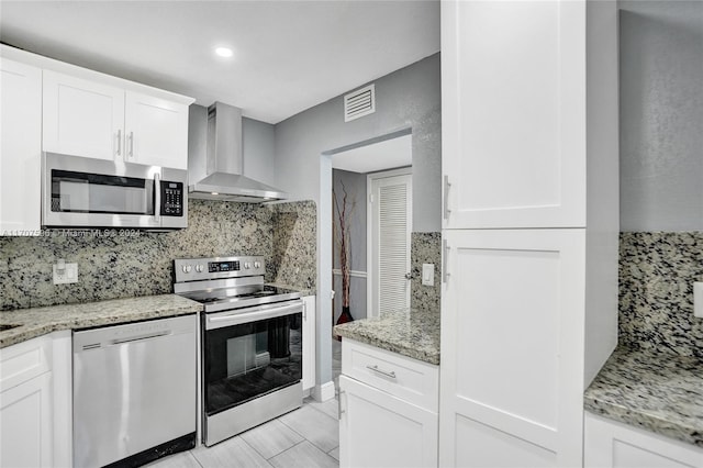 kitchen featuring white cabinets, stainless steel appliances, light stone countertops, and wall chimney exhaust hood