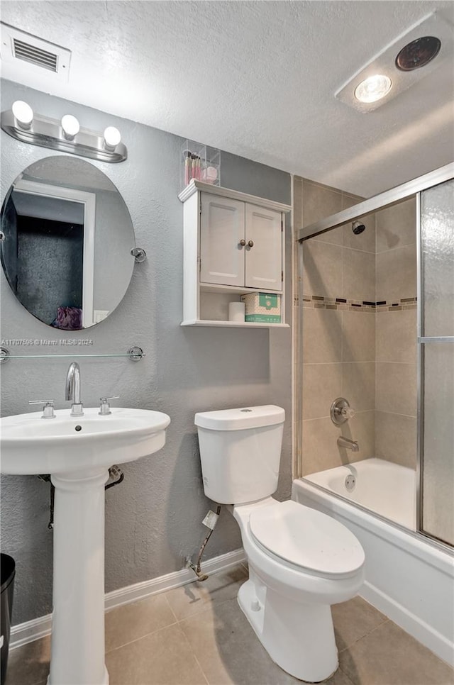 full bathroom featuring tile patterned floors, sink, bath / shower combo with glass door, toilet, and a textured ceiling