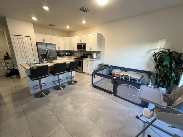 kitchen featuring a breakfast bar, decorative backsplash, an island with sink, white cabinetry, and stainless steel appliances