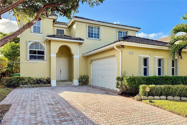 mediterranean / spanish house with a garage, a tiled roof, decorative driveway, and stucco siding