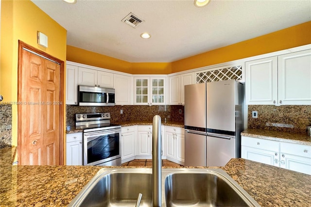 kitchen with white cabinetry, backsplash, dark stone counters, a textured ceiling, and appliances with stainless steel finishes