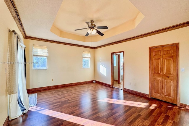 unfurnished room with ceiling fan, a healthy amount of sunlight, a raised ceiling, and dark wood-type flooring