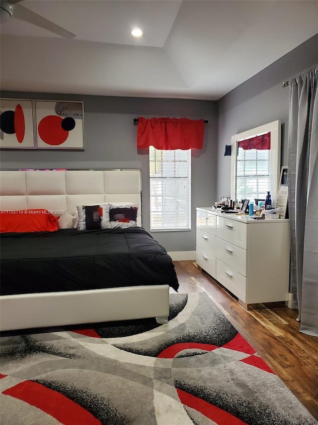 bedroom with hardwood / wood-style floors, ceiling fan, and a raised ceiling