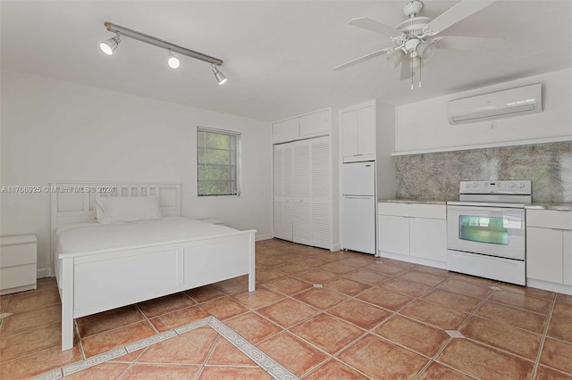 unfurnished bedroom featuring rail lighting, a wall unit AC, ceiling fan, white fridge, and a closet