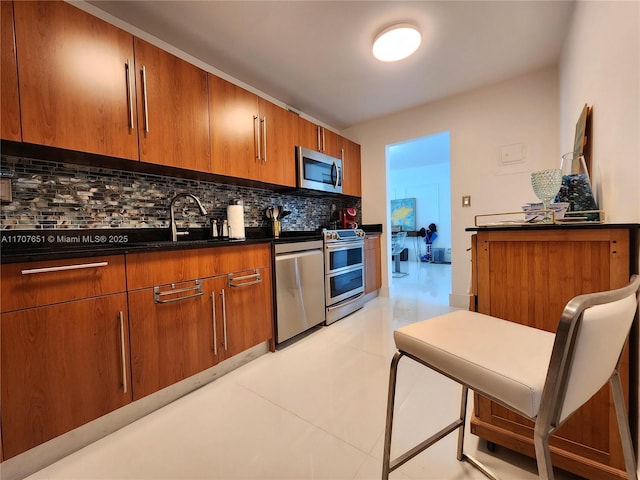 kitchen with dark countertops, a sink, stainless steel appliances, brown cabinets, and backsplash