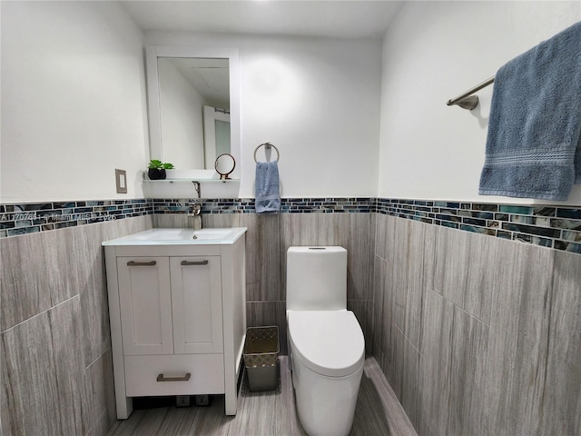 bathroom featuring vanity, toilet, wood finished floors, wainscoting, and tile walls