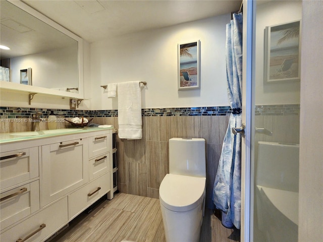 bathroom with a shower with shower curtain, vanity, toilet, wainscoting, and tile walls