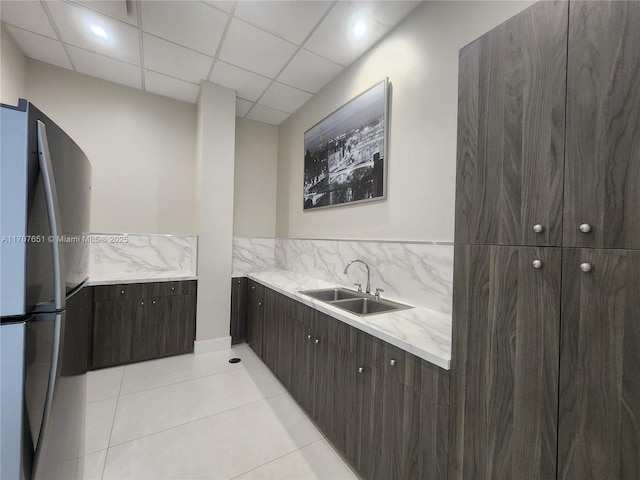 kitchen featuring dark brown cabinetry, light tile patterned floors, freestanding refrigerator, modern cabinets, and a sink