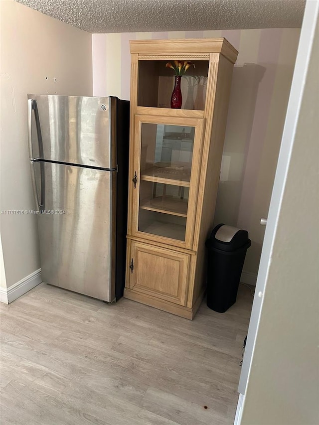 kitchen with stainless steel fridge, a textured ceiling, and light wood-type flooring