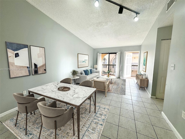 dining space with a textured ceiling, rail lighting, light tile patterned floors, and vaulted ceiling