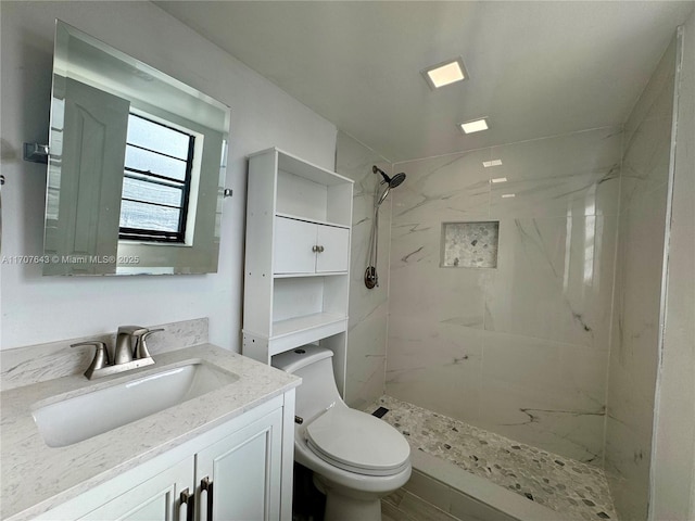 bathroom with a tile shower, vanity, and toilet