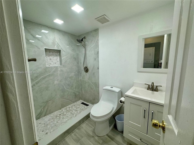 bathroom featuring toilet, a tile shower, and vanity