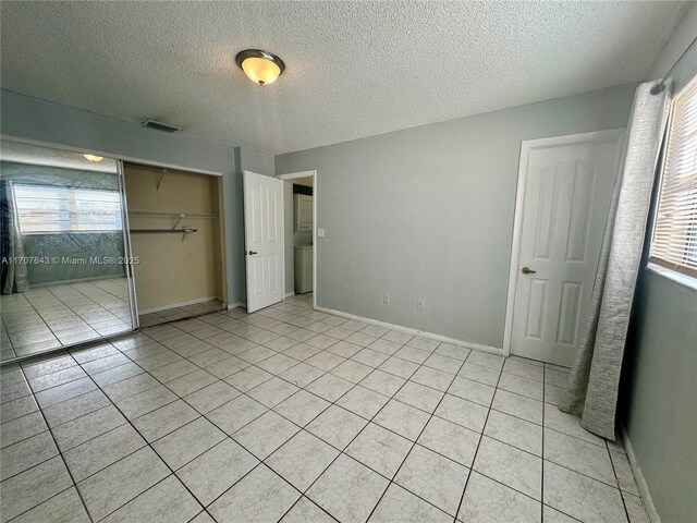 unfurnished bedroom featuring multiple windows, a closet, light tile patterned floors, and a textured ceiling