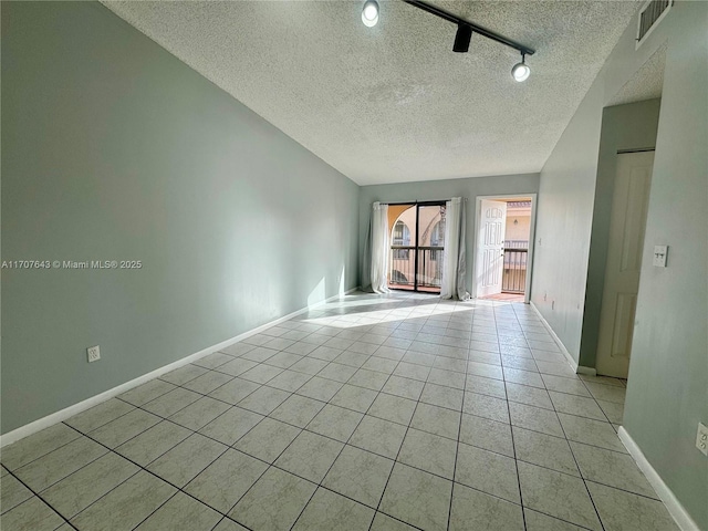 empty room featuring light tile patterned floors, rail lighting, and a textured ceiling