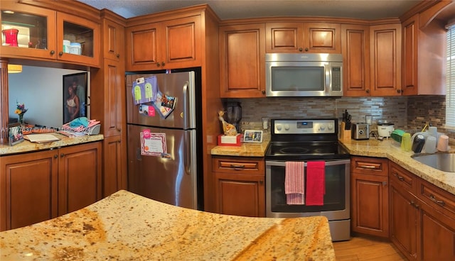 kitchen with decorative backsplash, light stone countertops, appliances with stainless steel finishes, and light hardwood / wood-style flooring