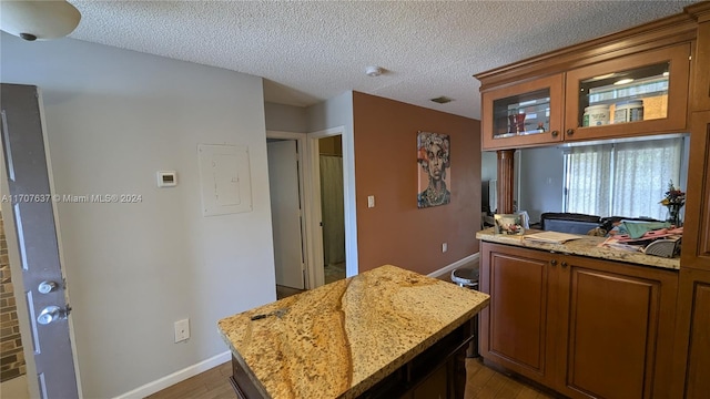 kitchen with light stone countertops, wood-type flooring, a textured ceiling, and a kitchen island