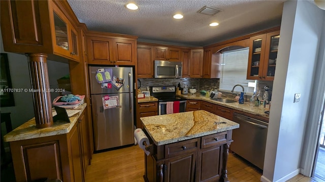 kitchen with backsplash, stainless steel appliances, sink, a center island, and light hardwood / wood-style floors