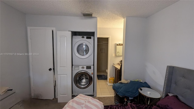 laundry area featuring light tile patterned floors, stacked washing maching and dryer, and a textured ceiling