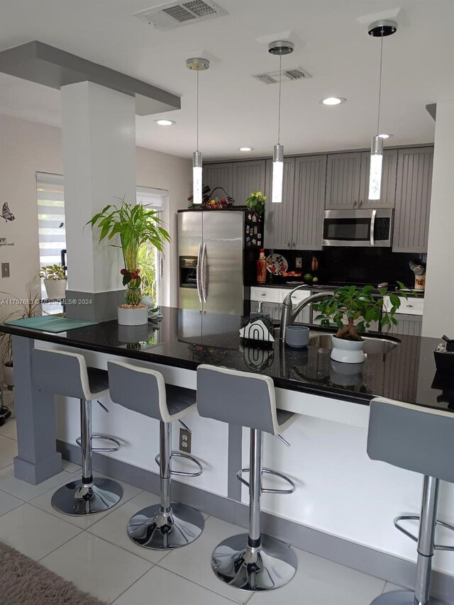 kitchen with decorative backsplash, stainless steel appliances, hanging light fixtures, and a breakfast bar area