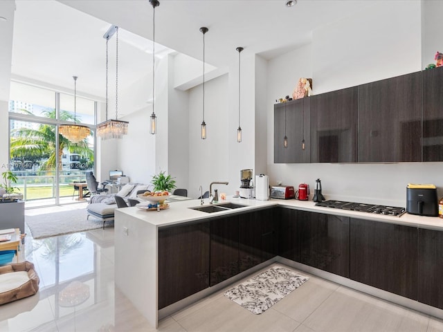 kitchen featuring dark brown cabinets, decorative light fixtures, stainless steel gas stovetop, and sink