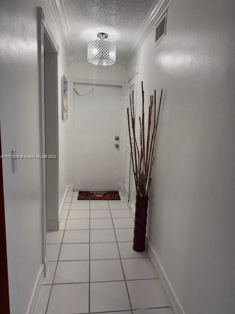 hallway with a textured ceiling, light tile patterned flooring, and crown molding