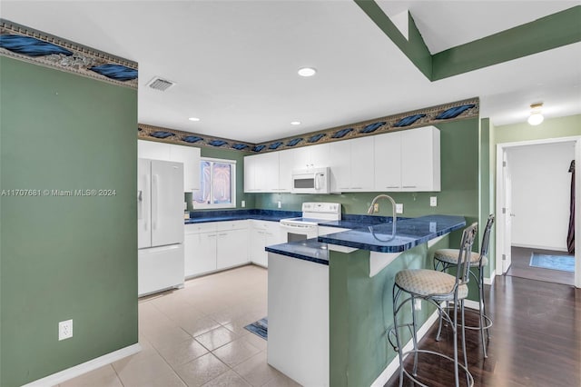 kitchen featuring white cabinetry, light hardwood / wood-style flooring, kitchen peninsula, white appliances, and a breakfast bar area