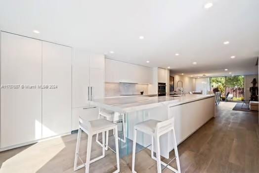 kitchen featuring a kitchen bar, white cabinetry, a spacious island, and wood-type flooring