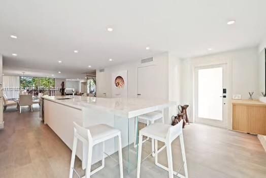 kitchen featuring a kitchen bar, light wood-type flooring, a spacious island, sink, and white cabinets