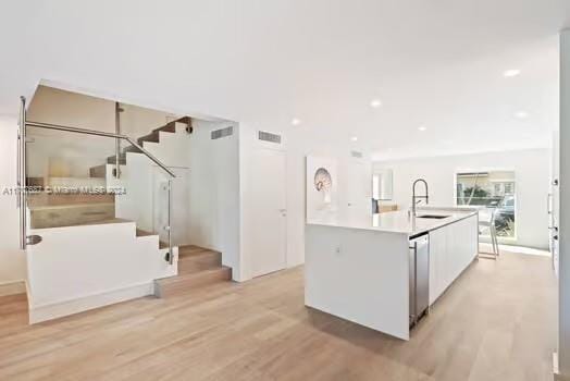 kitchen with white cabinetry, sink, light hardwood / wood-style flooring, stainless steel dishwasher, and a center island with sink