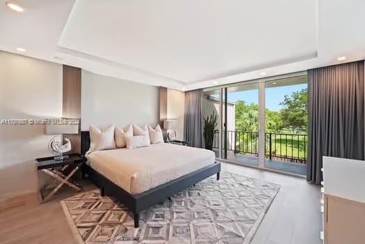 bedroom featuring a raised ceiling, light wood-type flooring, and access to outside