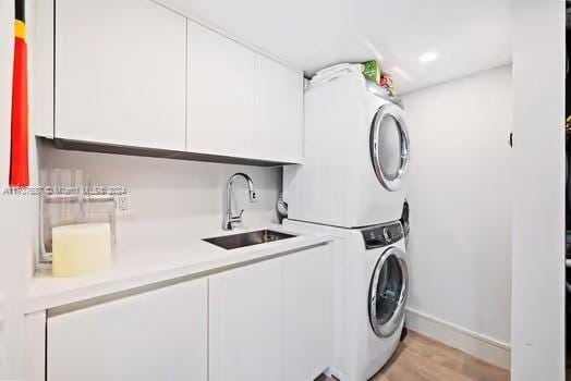 laundry room featuring stacked washing maching and dryer, sink, cabinets, and light hardwood / wood-style flooring