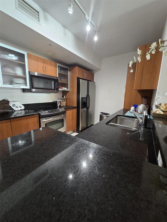 kitchen featuring sink, dark stone counters, track lighting, and appliances with stainless steel finishes