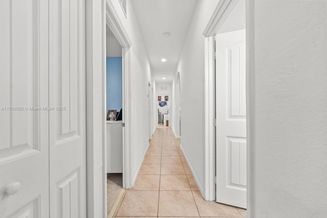 corridor featuring recessed lighting, light tile patterned flooring, a textured wall, and baseboards