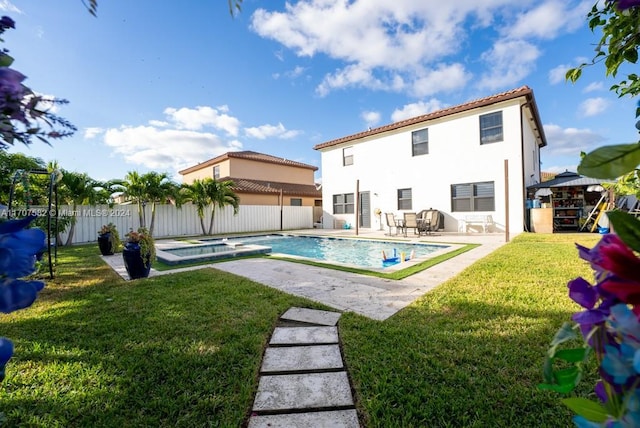 rear view of property with a swimming pool with hot tub, a yard, and a patio area