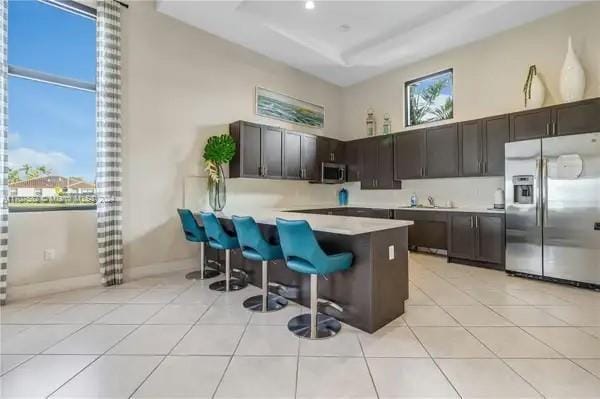 kitchen with kitchen peninsula, appliances with stainless steel finishes, a breakfast bar, dark brown cabinets, and a high ceiling