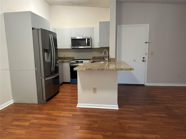 kitchen with stone counters, sink, kitchen peninsula, white cabinets, and appliances with stainless steel finishes