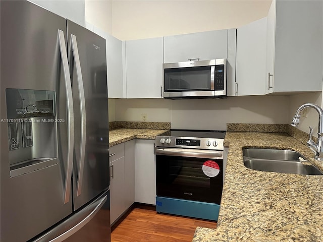 kitchen with sink, light stone countertops, appliances with stainless steel finishes, dark hardwood / wood-style flooring, and white cabinetry