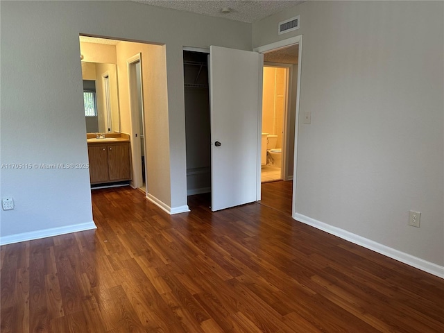 unfurnished bedroom featuring a walk in closet, ensuite bathroom, sink, dark hardwood / wood-style floors, and a closet