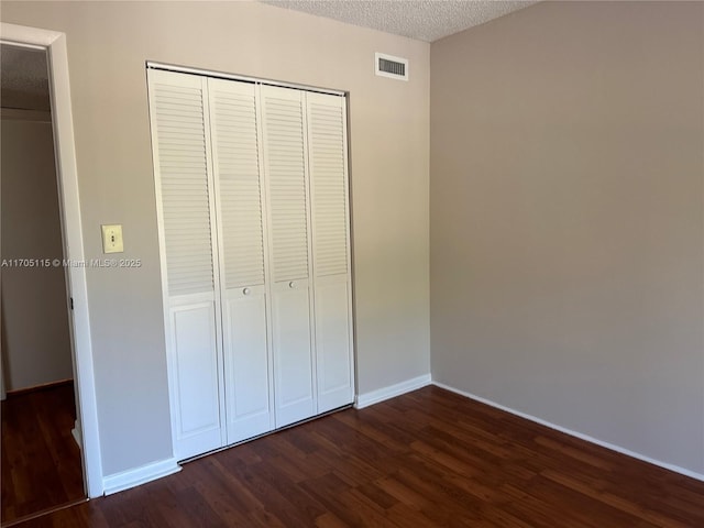 unfurnished bedroom featuring dark wood-type flooring, a textured ceiling, and a closet