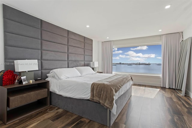 bedroom with dark hardwood / wood-style flooring and a water view