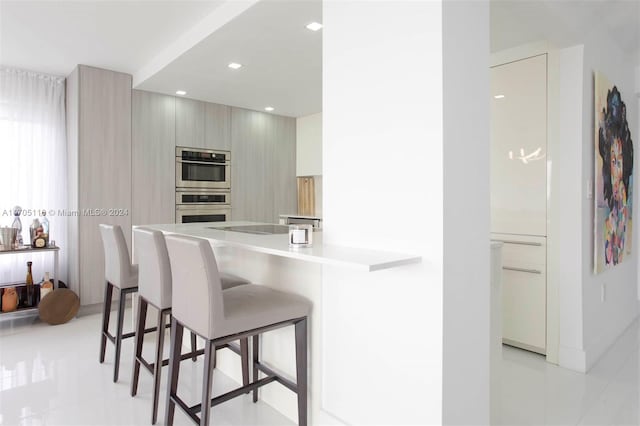 kitchen with kitchen peninsula, a kitchen breakfast bar, light tile patterned floors, and appliances with stainless steel finishes