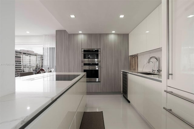 kitchen featuring black electric stovetop, sink, light stone countertops, stainless steel double oven, and beverage cooler