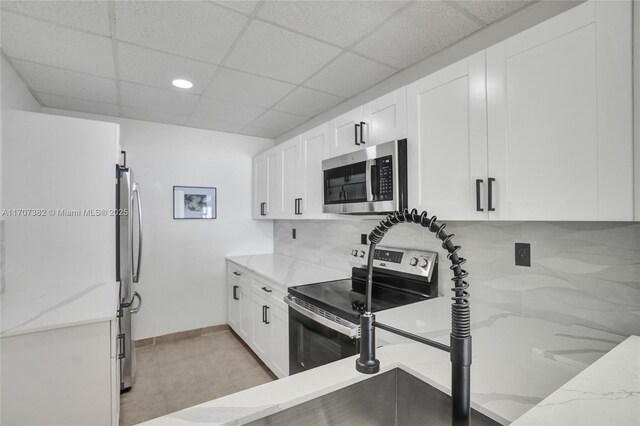 500 Bayview Dr Unit 118, Sunny Isles Beach, FL 33160 - kitchen with stainless steel appliances, decorative backsplash, light stone counters, white cabinets, and a drop ceiling