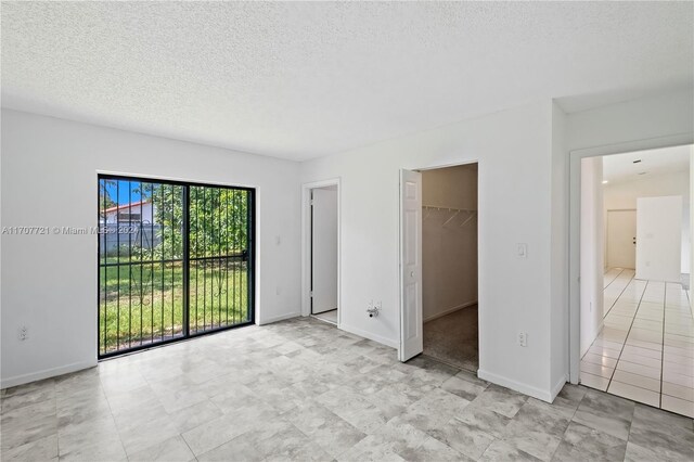 unfurnished bedroom featuring a spacious closet, a textured ceiling, access to outside, a closet, and light tile patterned floors