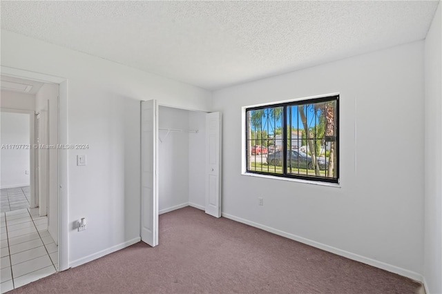 unfurnished bedroom with light colored carpet, a textured ceiling, and a closet