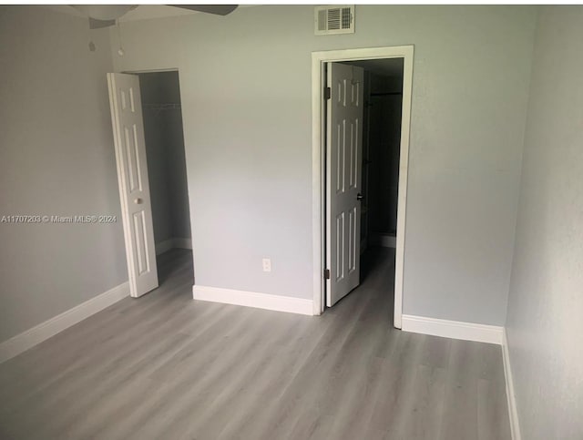 unfurnished bedroom with a walk in closet, a closet, light hardwood / wood-style flooring, and ceiling fan