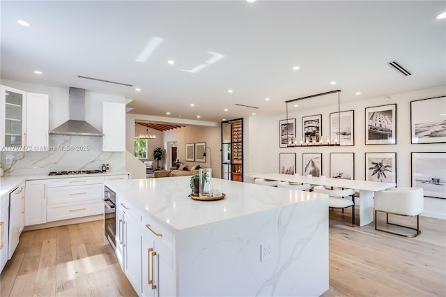 kitchen featuring decorative backsplash, light stone countertops, wall chimney exhaust hood, stainless steel gas cooktop, and a kitchen island