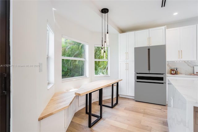 kitchen with light stone countertops, stainless steel fridge, white cabinets, light hardwood / wood-style floors, and hanging light fixtures